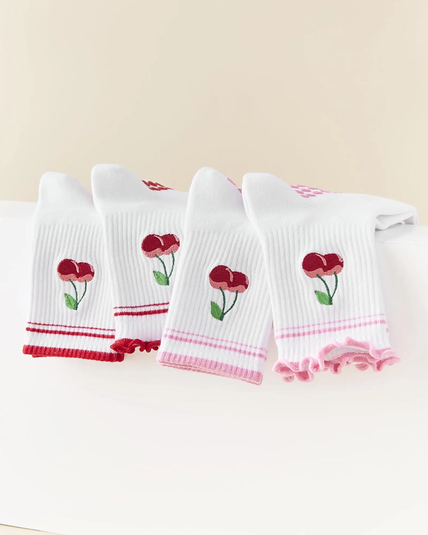 Set of four white socks with red floral designs on a beige background