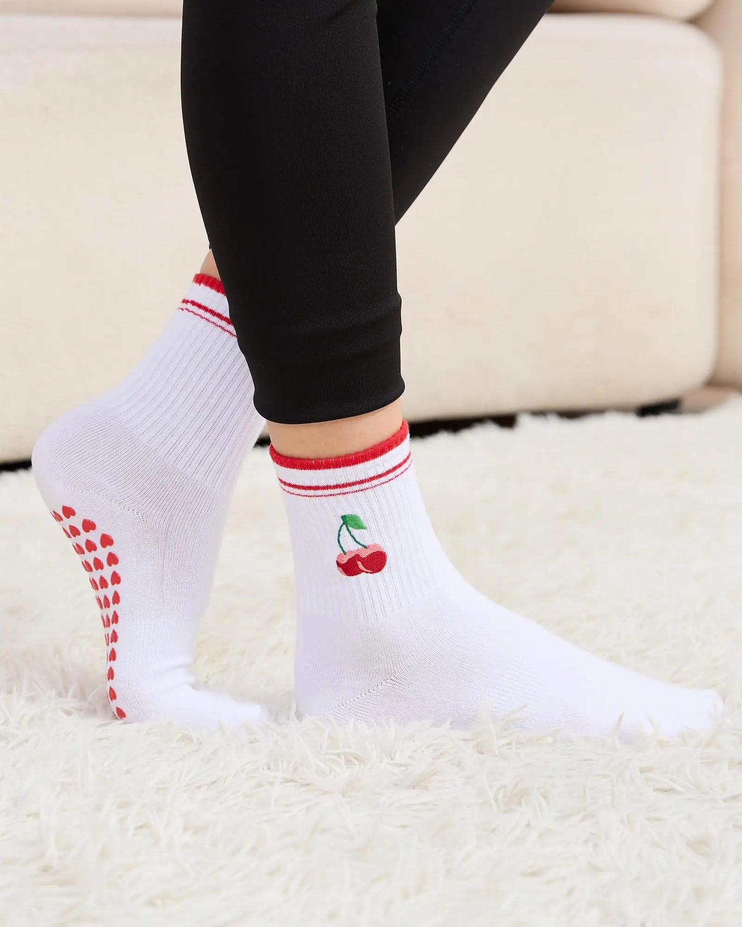White socks with red accents and cherry design worn by a person on a light-colored surface.
