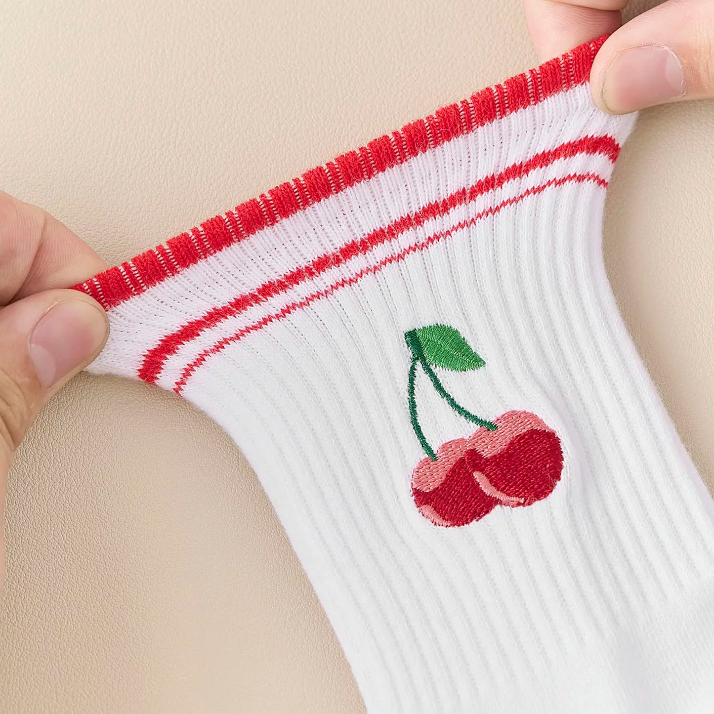 White sock with red trim and embroidered cherries held by a hand against a beige background