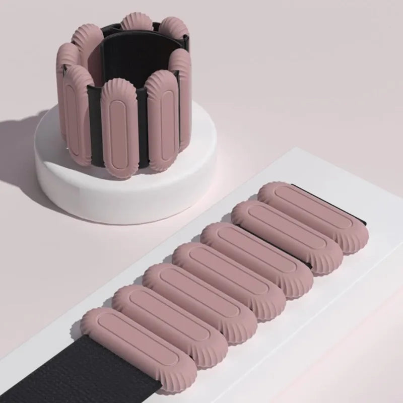 Pink ankle or wrist weights on a white stand with ankle or wrist weight on a light pink background

